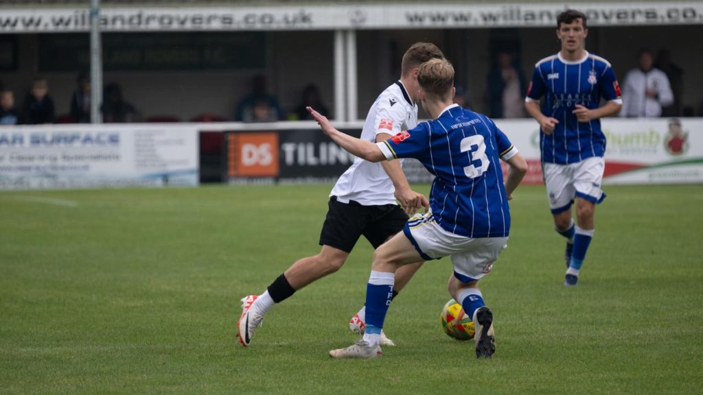 Footballer in a blue shirt tackling a player in a white shirt
